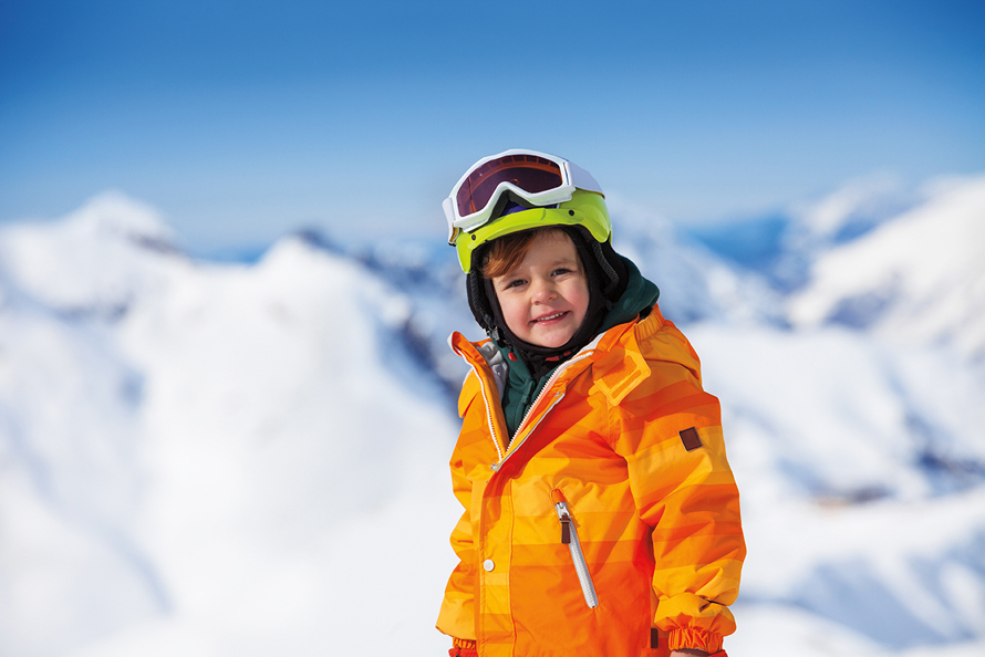 boy wearing winter gear on top of a mountain with the blue sky in the background