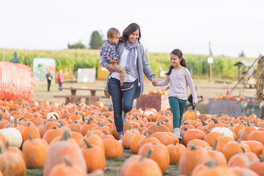 mom with daughters in pumpkin patch istock
