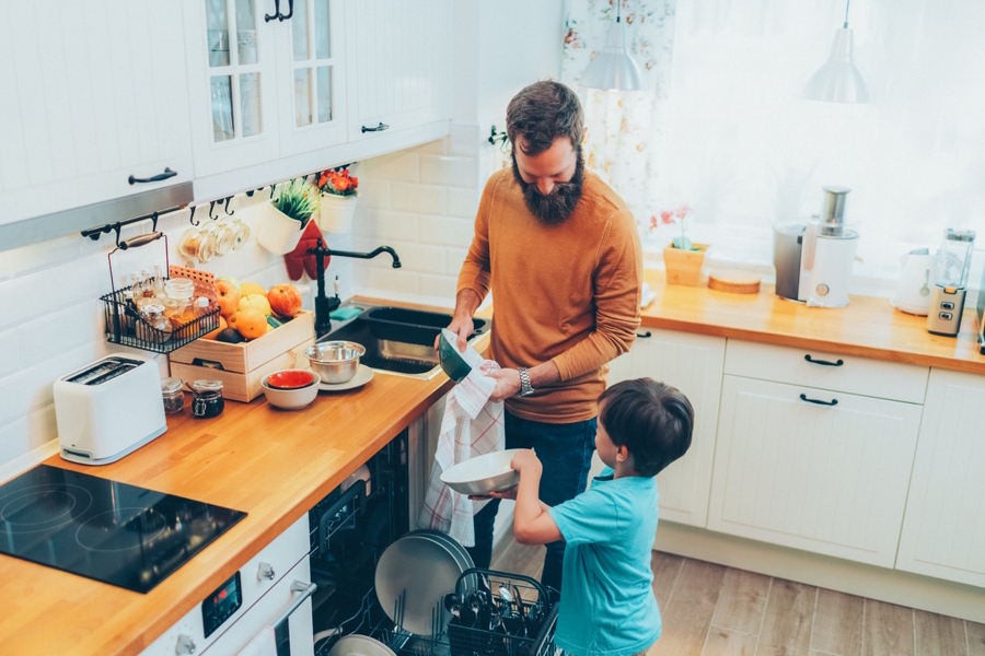 a son helps his dad unload a dishwasher, as part of a new family routine habit