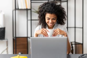 Woman holding coffee and smiling at laptop