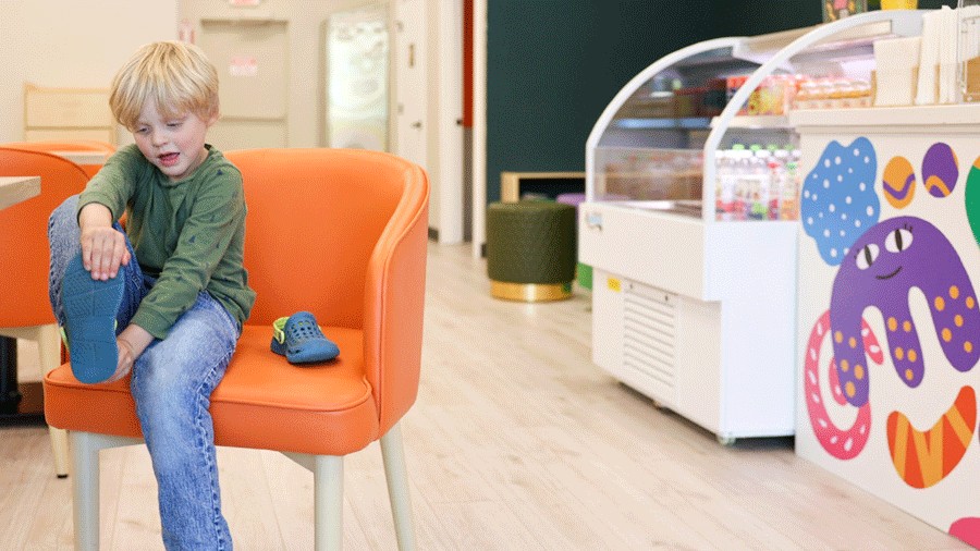 kid taking off his shoes at Nixi City for indoor playtime, with snacks and seating int the background