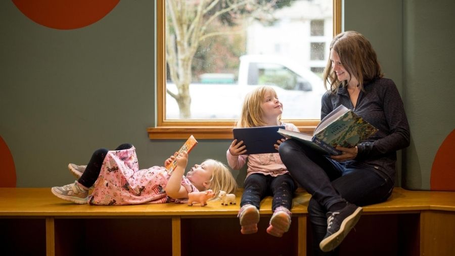 parent and kids reading by the window of a library