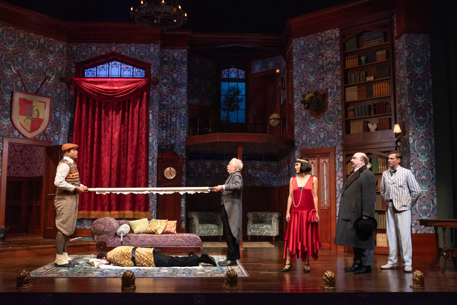 Cast of the play attempting to move a dead body, who keeps moving around on his own