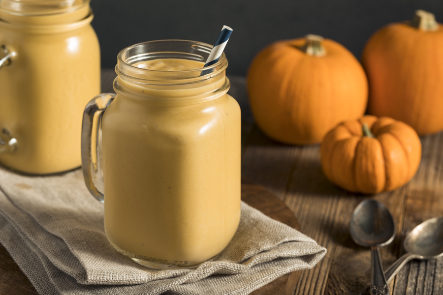 Pumpkin smoothie in a jar with pumpkins behind it