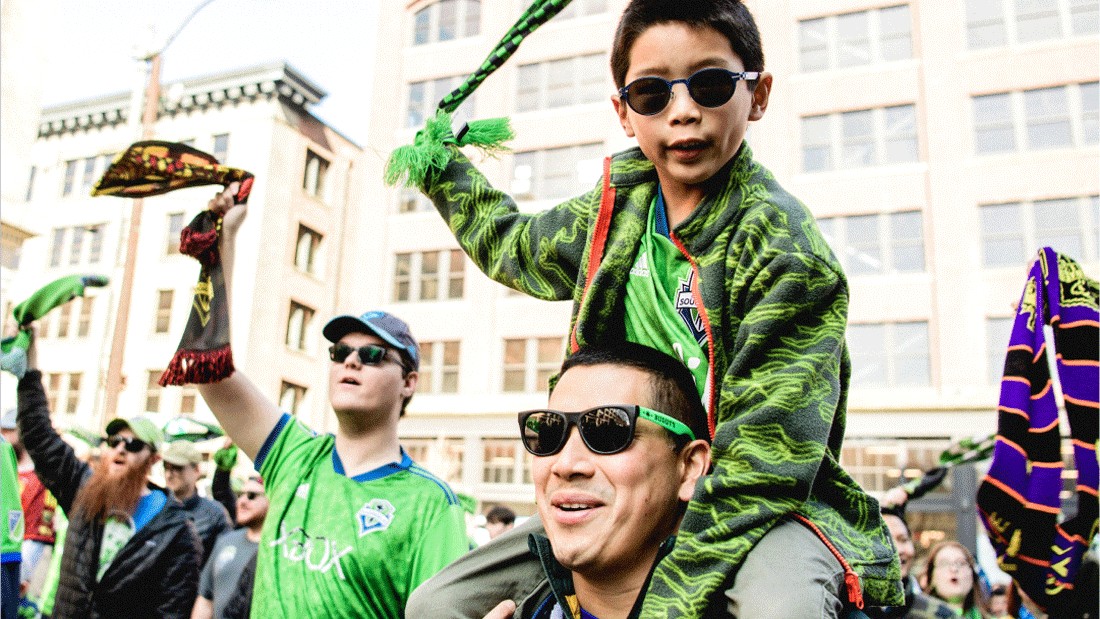 boy on man's shoulders wearing sounders fan attire cheering on the team for the FIFA Club World Cup in Seattle