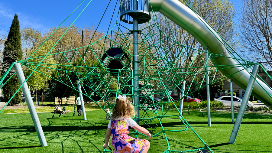 young girl climbing up green rope climber toward a metal tube slide at South Park Community Center in Seattle