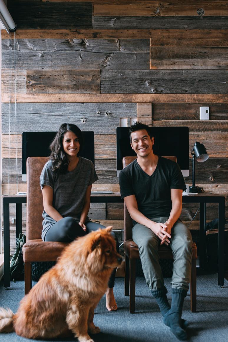 A smiling young couple and their dog relax in a living room