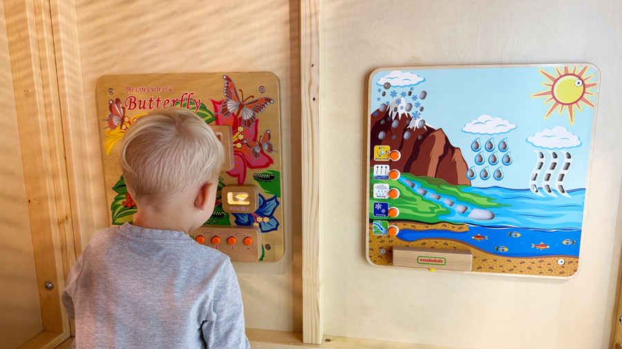 young boy playing with interactive busy boards on the wall