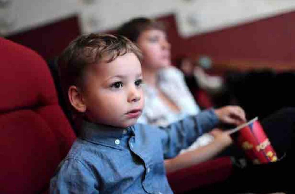 Boy in a blue shirt eating popcorn in a movie theater