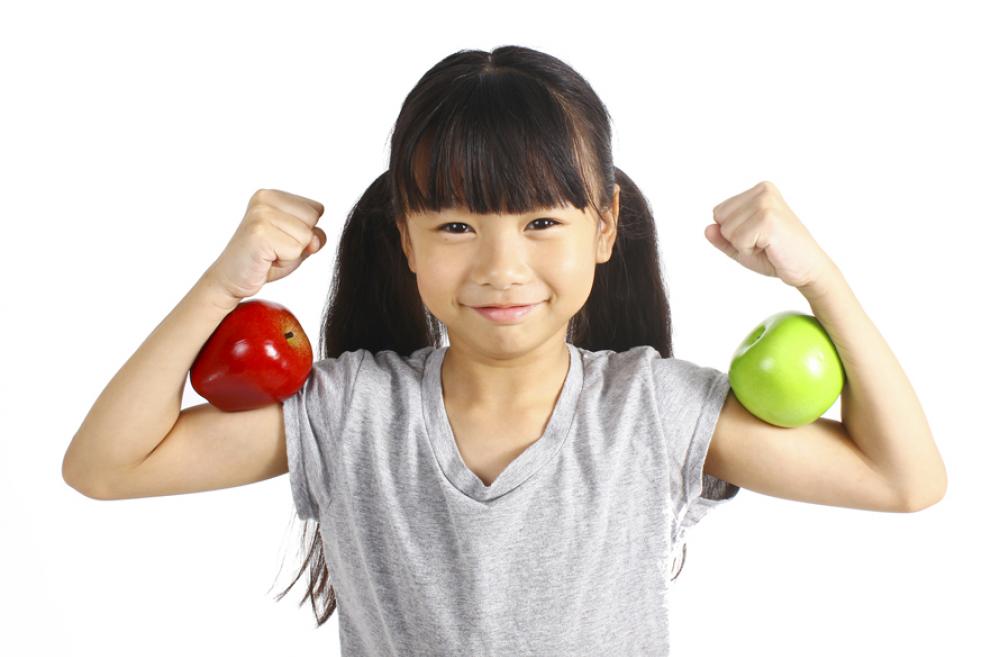 little girl holding her arms up to show off her biceps, with apples balanced on her arms