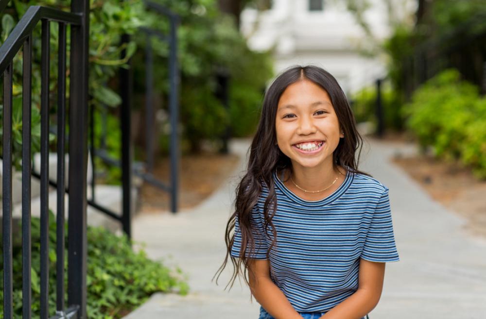 girl standing outside on a sidewalk smiling