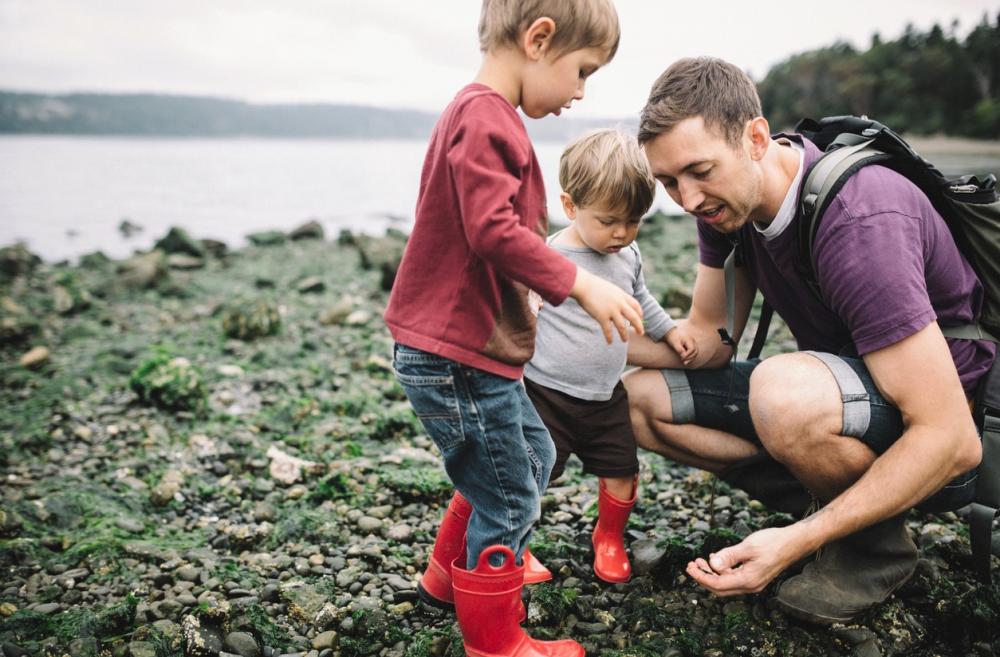 Dad and two little kids looking at rocky beach and tide pool finds