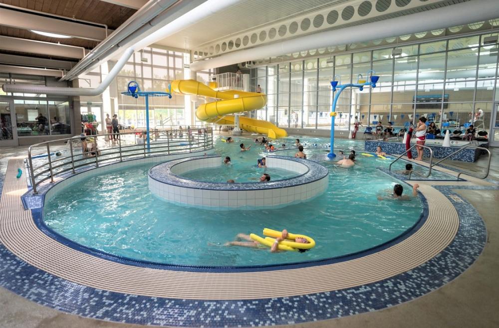 View of people swimming in Rainier Beach Pool in Seattle. Yellow twister slide is in the backgorund and the lazy river feature is in the foreground