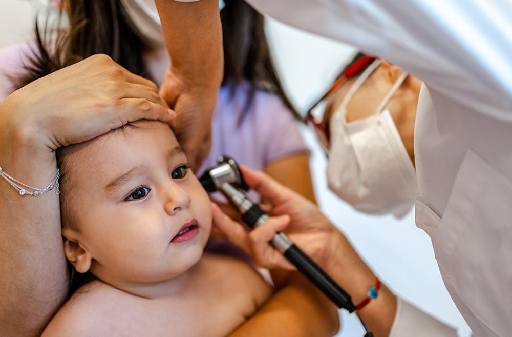 Mother holds child as doctor check their ears.