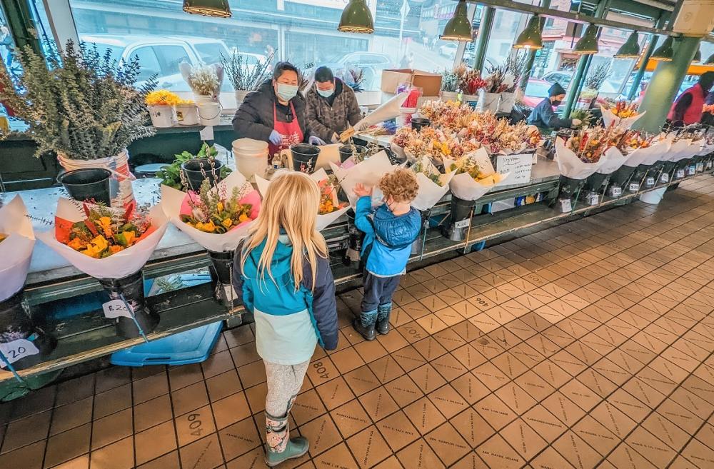 Kids look at flower bouquets at Pike Place Market and talk with a flower vendor best family stops at Seattle's Pike Place Markeet