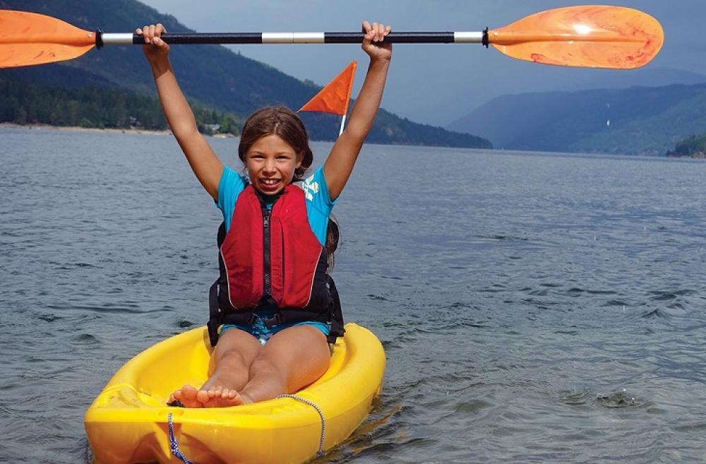 Girl in a canoe with paddle raised over her head