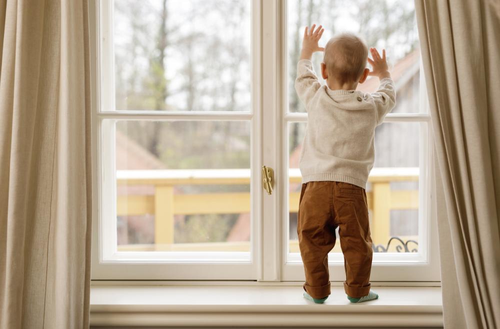 Child standing on a window ledge looking out 
