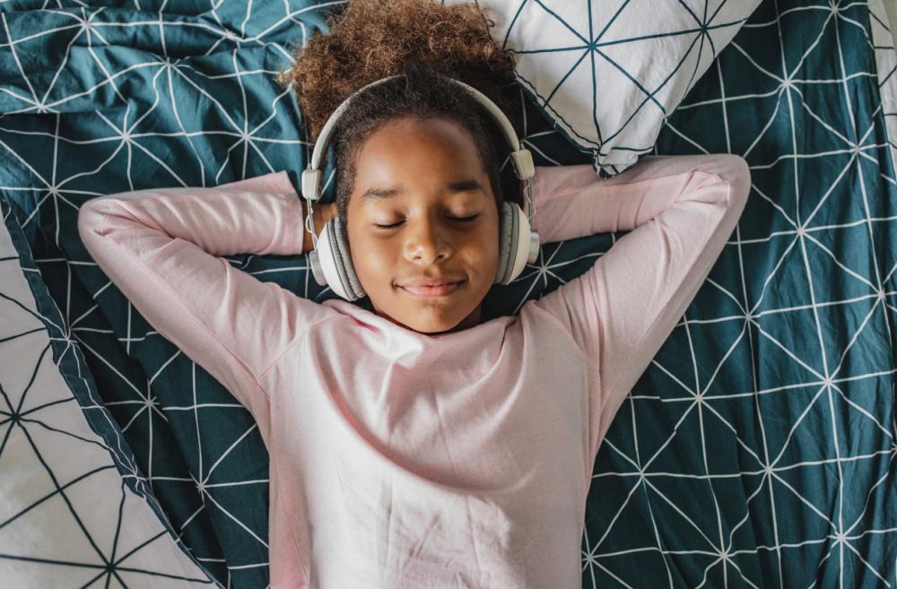 Girl lying in bed with headphones on listening and relaxing 