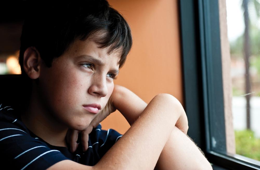 Young boy looking out a window looking sad