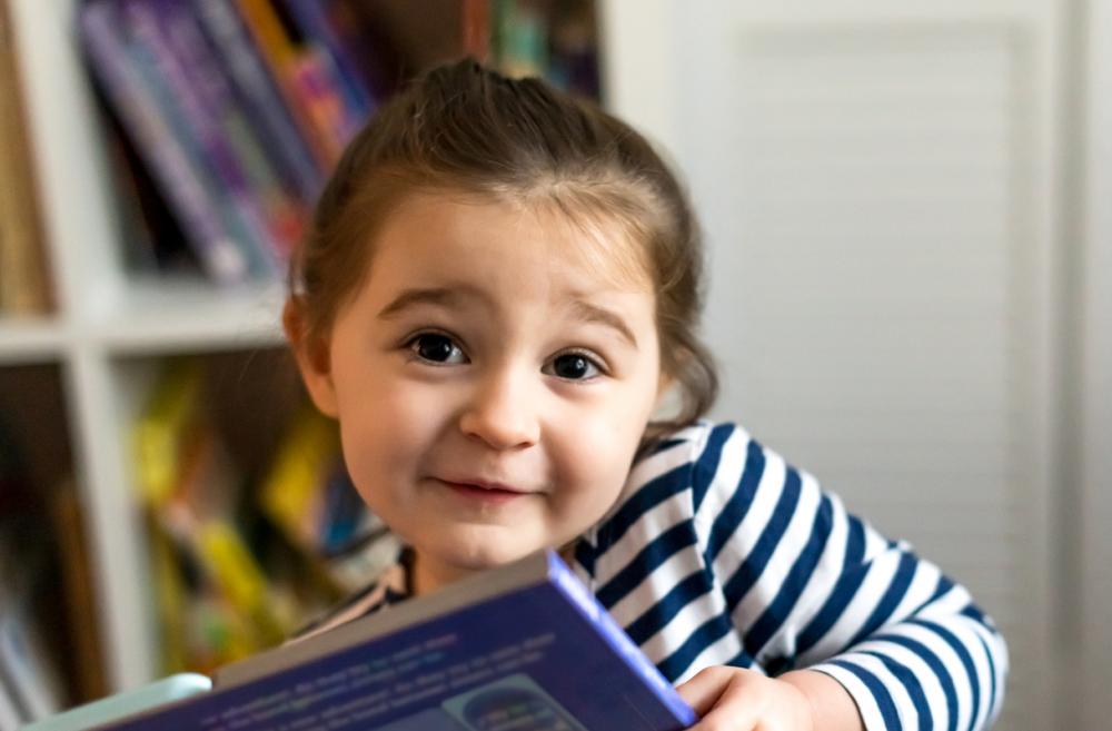 A smiling little girl in a striped shirt holds a picture book