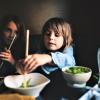 Two kids are eating in a restaurant with their family trying new foods using chopsticks best global dining destinations Seattle families