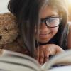 Girl cuddling stuffed bear, smiling and reading a book series for kids