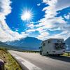 A small RV drives on a road past a lake with mountains in the background sun and clouds in blue sky best family road trip routes itineraries from seattle