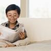 Young boy wearing glasses sitting on a couch reading a newspaper