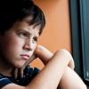 Young boy looking out a window looking sad