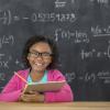 Young girl holding a clipboard sitting in front of a chalk board with math written on it