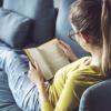 Teenage girl sits on a blue couch reading a novel