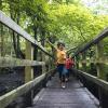 Two boys brothers run across a wooden bridge in the woods on a spring hike near Seattle best spring hikes for kids families around Seattle Puget Sound