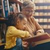 Grandma and child sitting on the floor of a library reading a book 