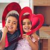 Two kids with paper hearts by their faces and useful Valentine's Day favors