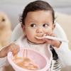 Baby in a highchair holding an empty bowl and spoon as a way to wean baby to solid foods
