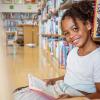 little girl sitting in the library reading a book