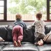 two kids sitting on a couch looking outside