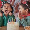 An excited child wearing a costume sits in front of cake at a toddler birthday