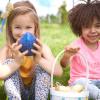 Two girls sitting on grass, holding eggs and basket for Easter.