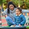 mom playing with child on swing at playground