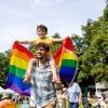 A young boy holds a Pride rainbow flag while on his father's shoulders to celebrate Pride.