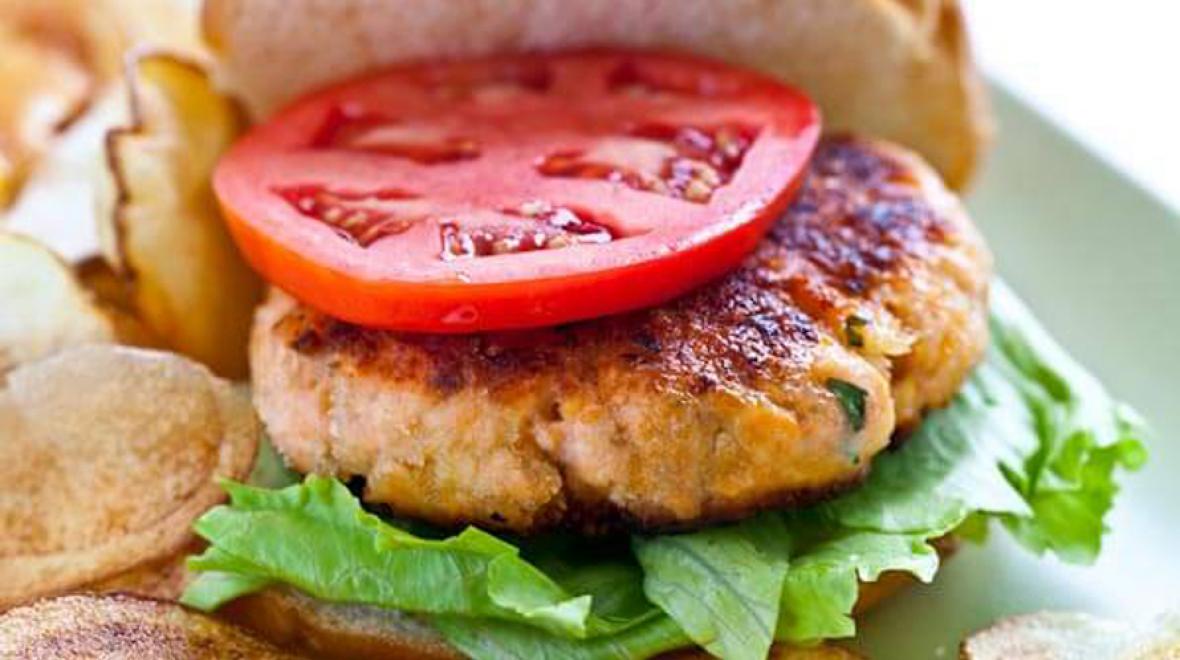salmon burger on a plate with a slice of tomato and lettuce on a bun