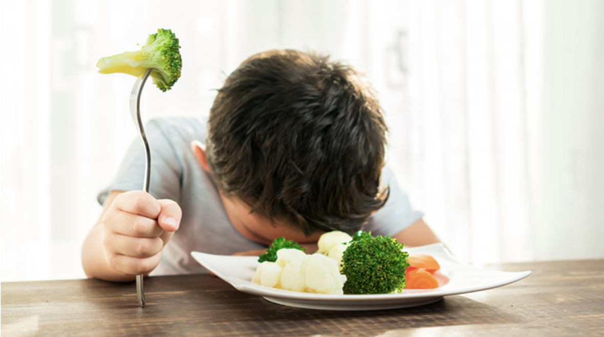 Kid with vegetables at dinner table