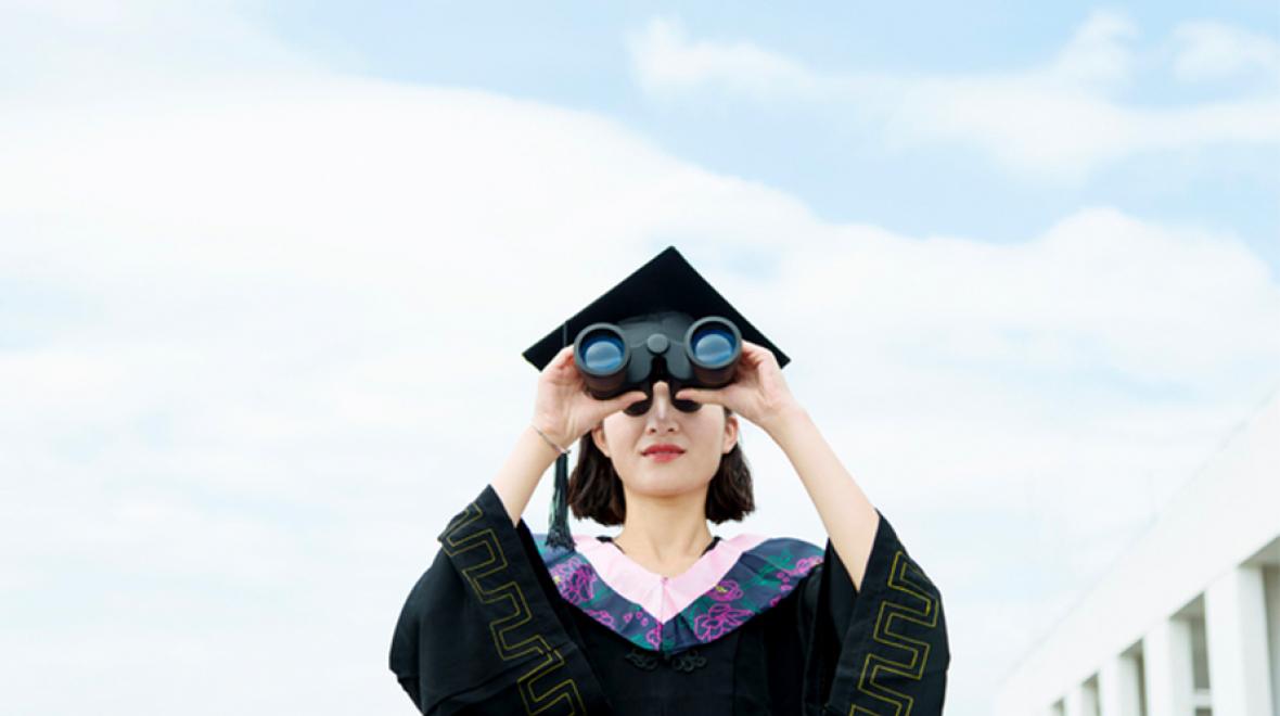 Young woman graduate looking through binoculars 