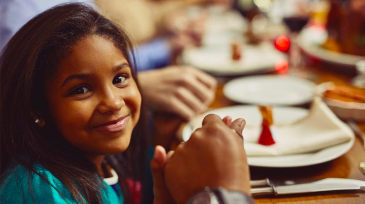 Smiling young girl holding hands at dinner table
