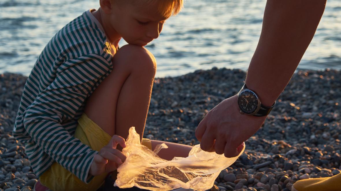 A young boy helps his father collect garbage on the beach at sunset 