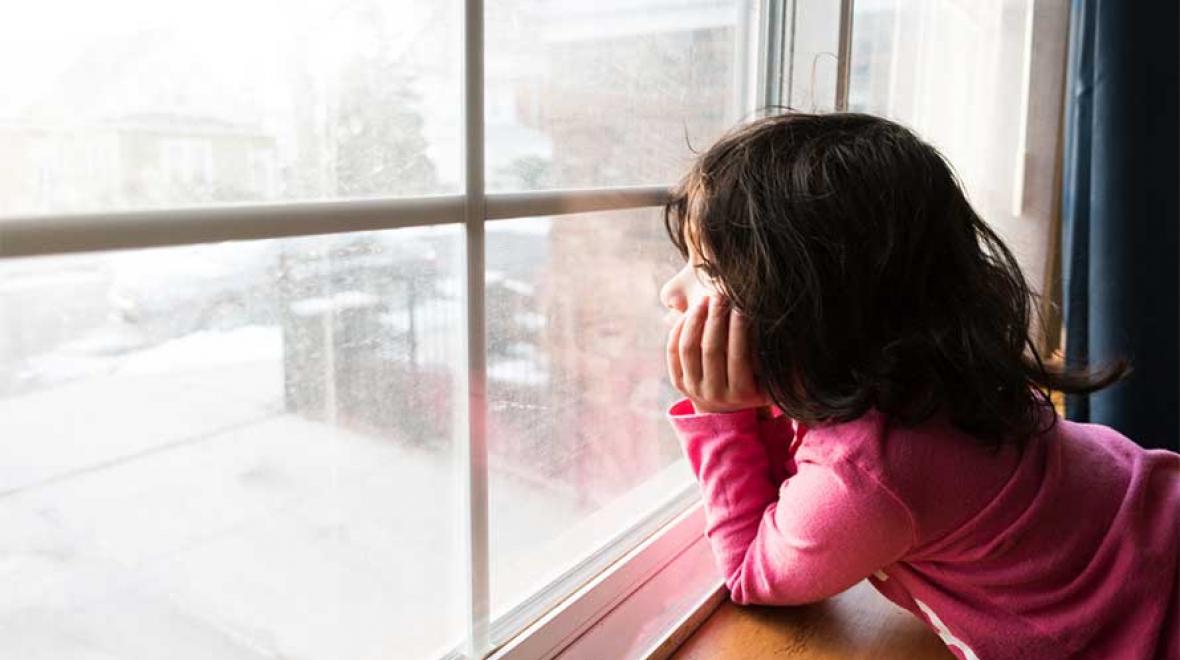 kid looks out the window at the snow