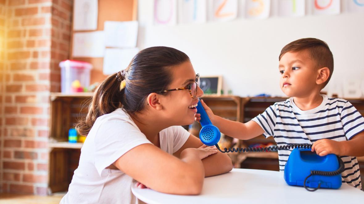 little boy holding a blue phone up to his preschool teacher's ear