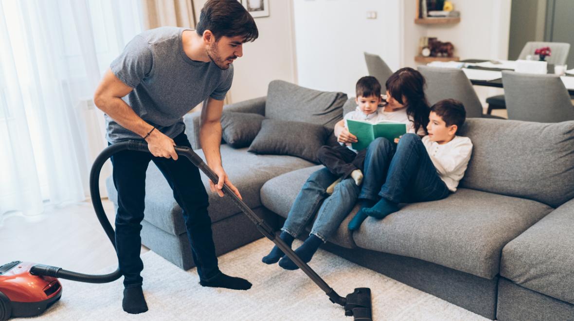 Father vacuums while mother reads a book to their kids