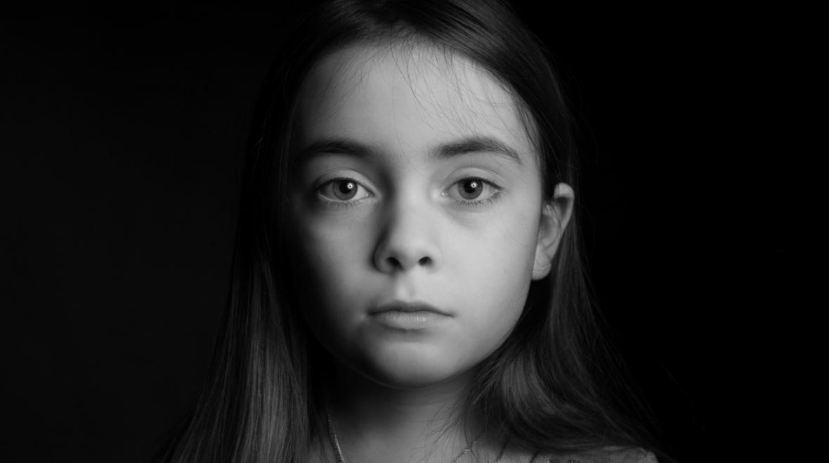 black and white photo of a serious girl partially in shadow looking at the camera